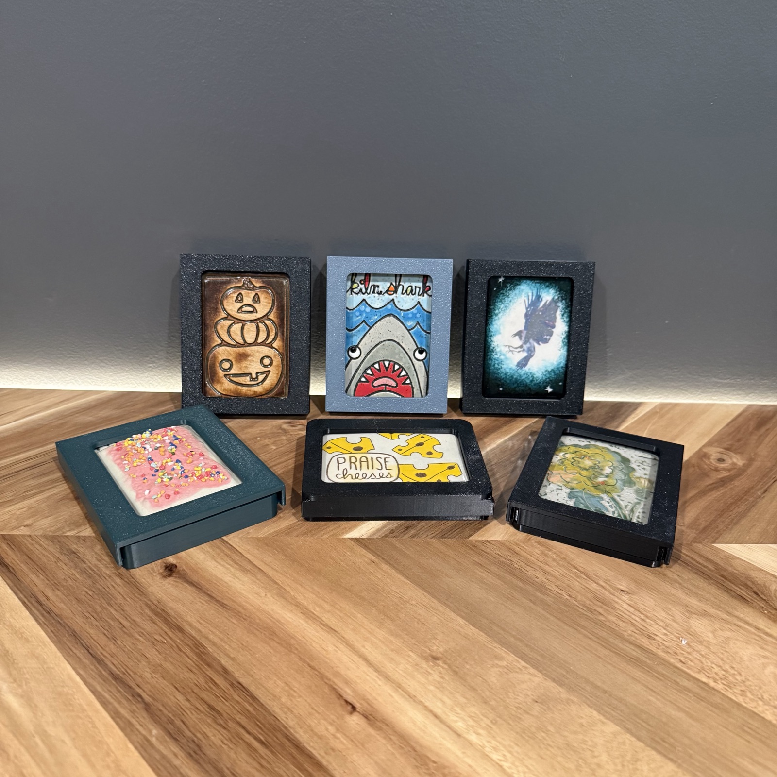 Six single ATC display frames in black, pale blue and green, holding ceramic and painted artist trading cards
